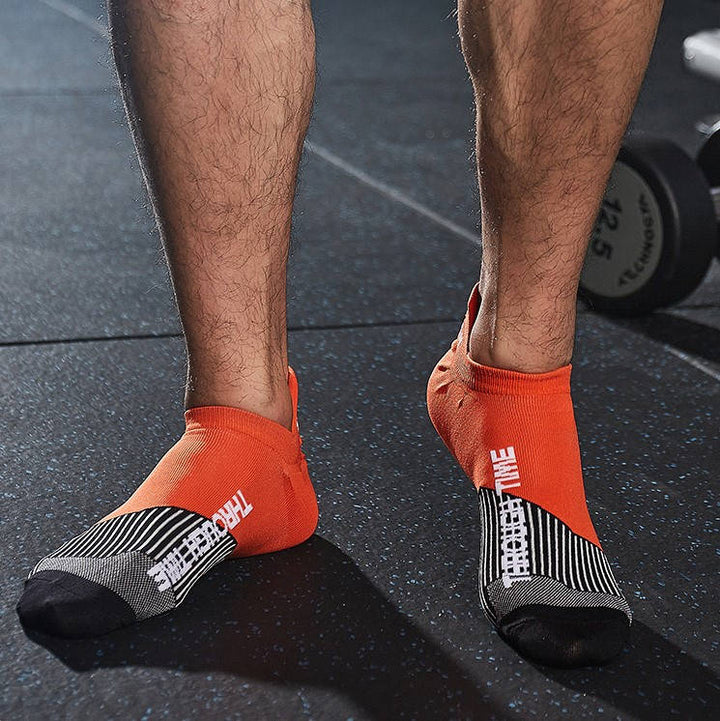 Athlete's feet in orange and grey ankle support socks in a gym environment.