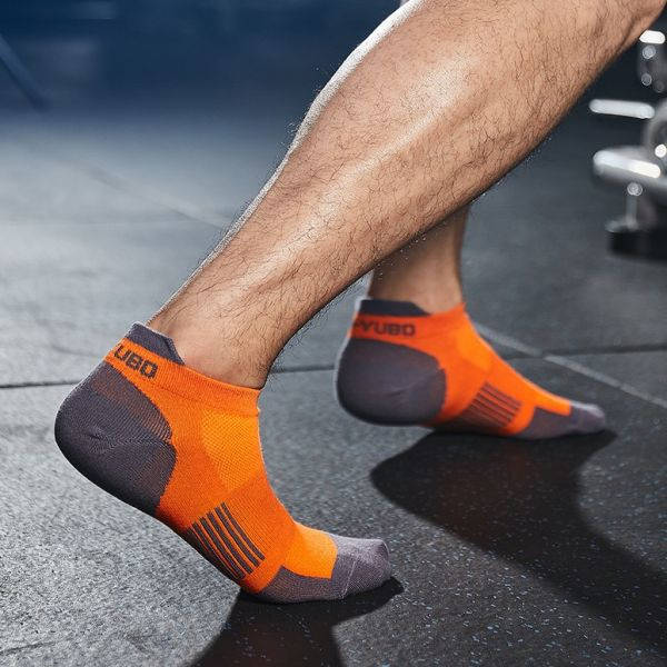 Athlete adjusting an orange and grey performance sock with reflective elements in a gym setting.