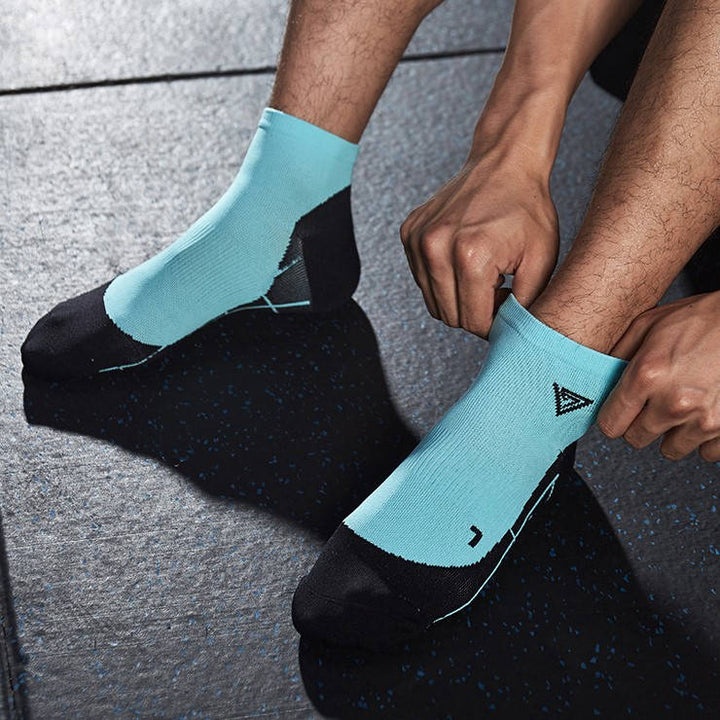 Person wearing turquoise and black athletic socks with a unique triangle logo, seated on a gym floor.