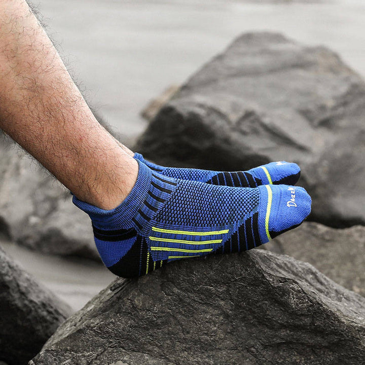 A person's foot in a blue toe sock with green stripes, resting on a rocky surface.