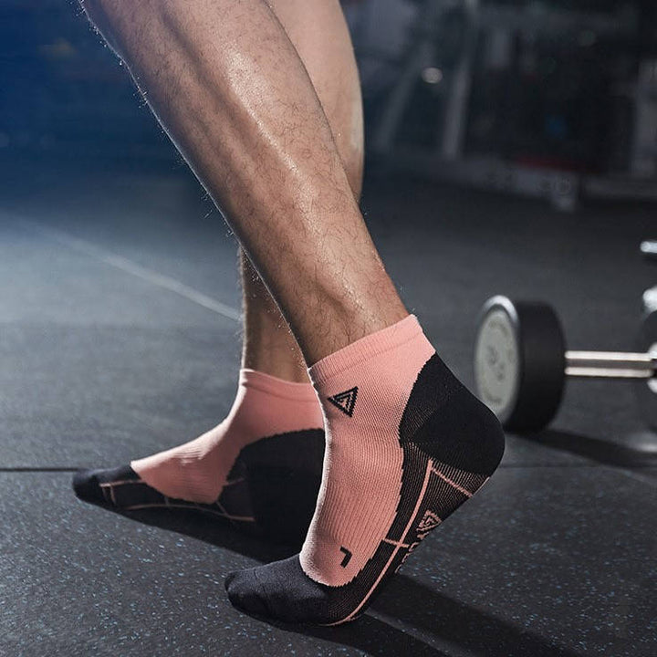 Close-up of coral and black sports socks on a person’s feet in a gym with weights in the background.