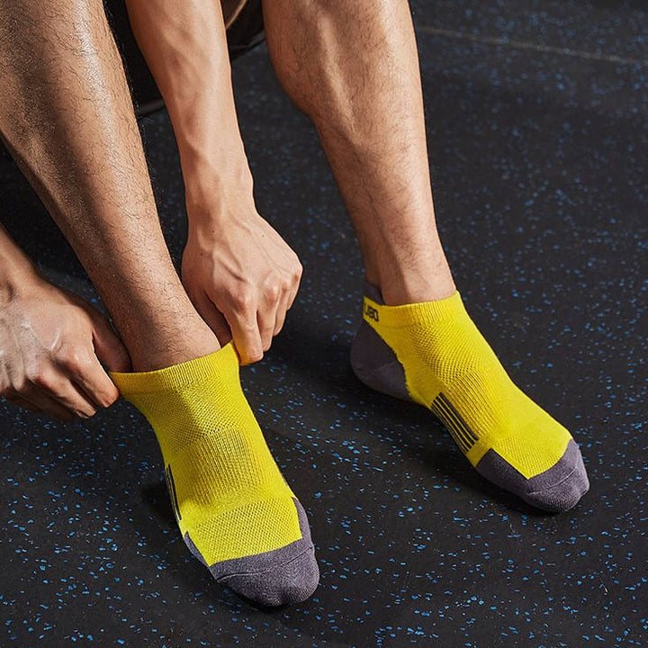 Person adjusting yellow and grey ankle socks in a gym setting.