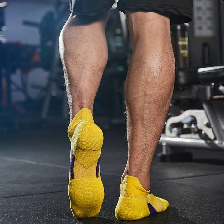 Person in a gym wearing yellow sports socks with purple accents, viewed from behind.