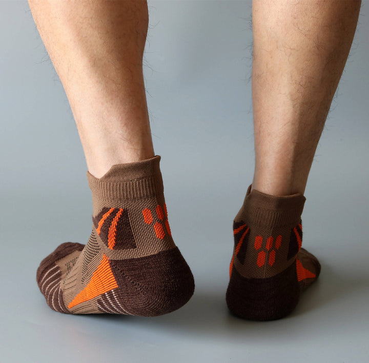 Person wearing brown ankle socks with orange pattern and non-slip grips on the heel.